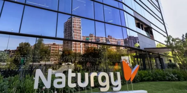 Front of a modern glass office building with a large Naturgy sign and orange logo in a landscaped area on a sunny day; reflections in the glass panels nearby.