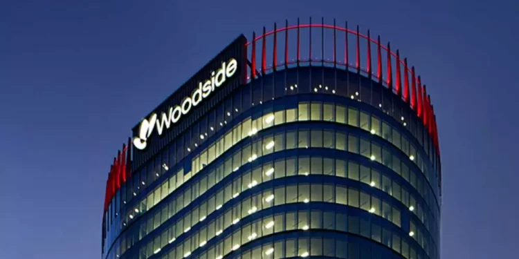 Cylindrical glass office tower at dusk with illuminated windows and a Woodside logo at the top-left.