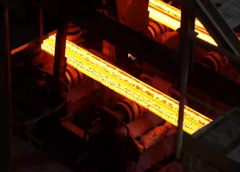 Glowing orange-hot steel bar on a roller conveyor in a metalworking facility.