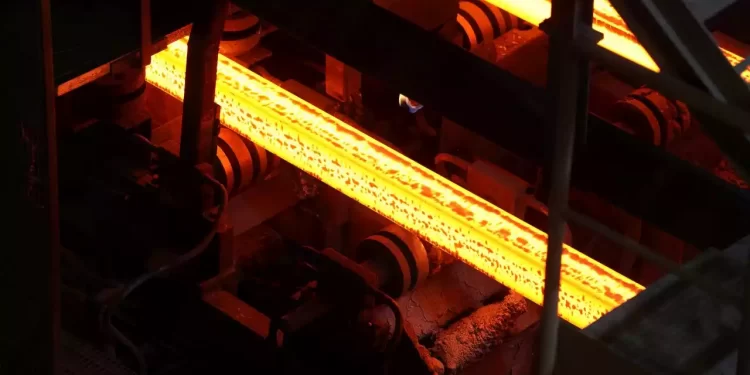 Glowing orange-hot steel bar on a roller conveyor in a metalworking facility.