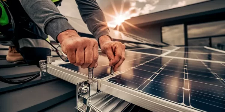 Technician tightening bolts on a solar panel installation on a roof at sunset