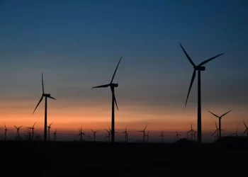 Silhouettes of wind turbines on a flat horizon at sunset with an orange-to-blue sky.