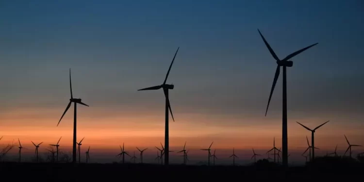 Silhouettes of wind turbines on a flat horizon at sunset with an orange-to-blue sky.