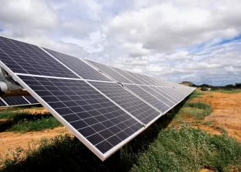 Row of tilted solar panels installed on a metal frame in a dry field under a cloudy sky (solar farm)