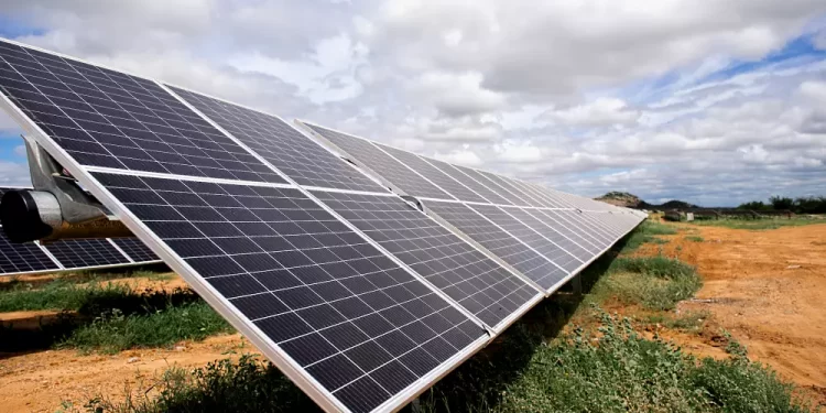 Row of tilted solar panels installed on a metal frame in a dry field under a cloudy sky (solar farm)