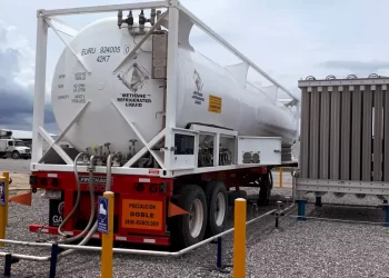 White methane refrigerated liquid tanker on a red semi-trailer, hoses connected at a loading site with safety barriers nearby.
