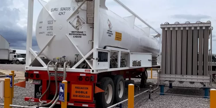 White methane refrigerated liquid tanker on a red semi-trailer, hoses connected at a loading site with safety barriers nearby.