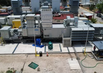 Industrial generator set on a transport trailer at a construction site, with stairs, ducts, and workers nearby