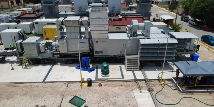 Industrial generator set on a transport trailer at a construction site, with stairs, ducts, and workers nearby