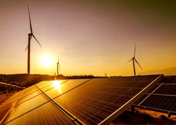 Solar panels in foreground with wind turbines on a hill at sunset, showcasing renewable energy site.