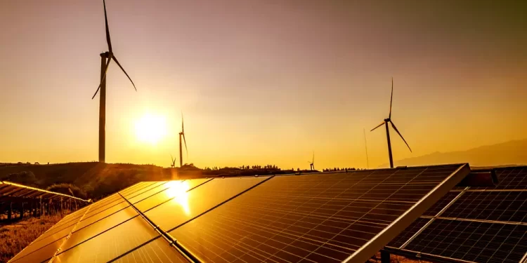 Solar panels in foreground with wind turbines on a hill at sunset, showcasing renewable energy site.