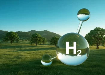 Large glass H2 molecule model on a sunny grassy field with trees and hills in the background, the big sphere labeled H2.