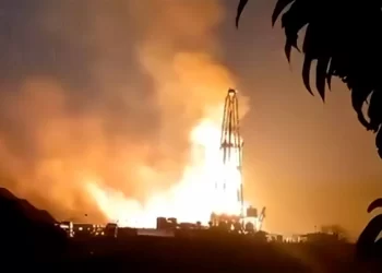 Rocket on a launchpad blasting flames into the night sky with a large plume of fire and smoke.