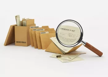 Row of tan archival folders with labeled dividers, a magnifying glass examines a document, plus scattered envelopes and clips.